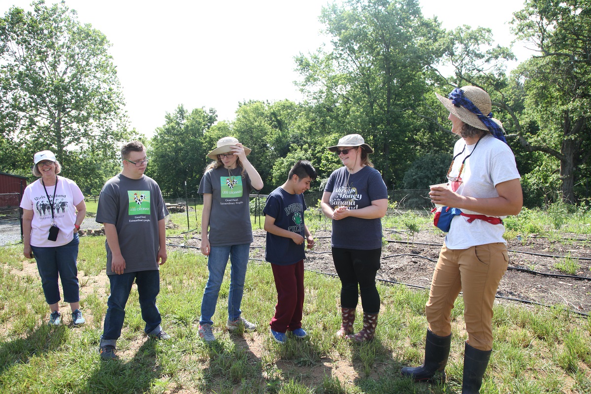 Group of people with AFLO shirts standing in the field.  Vegetable beds with drip tape are in the background