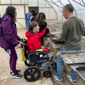Homefields1 People working in a greenhouse. One person in a red jacket is in a wheel chair